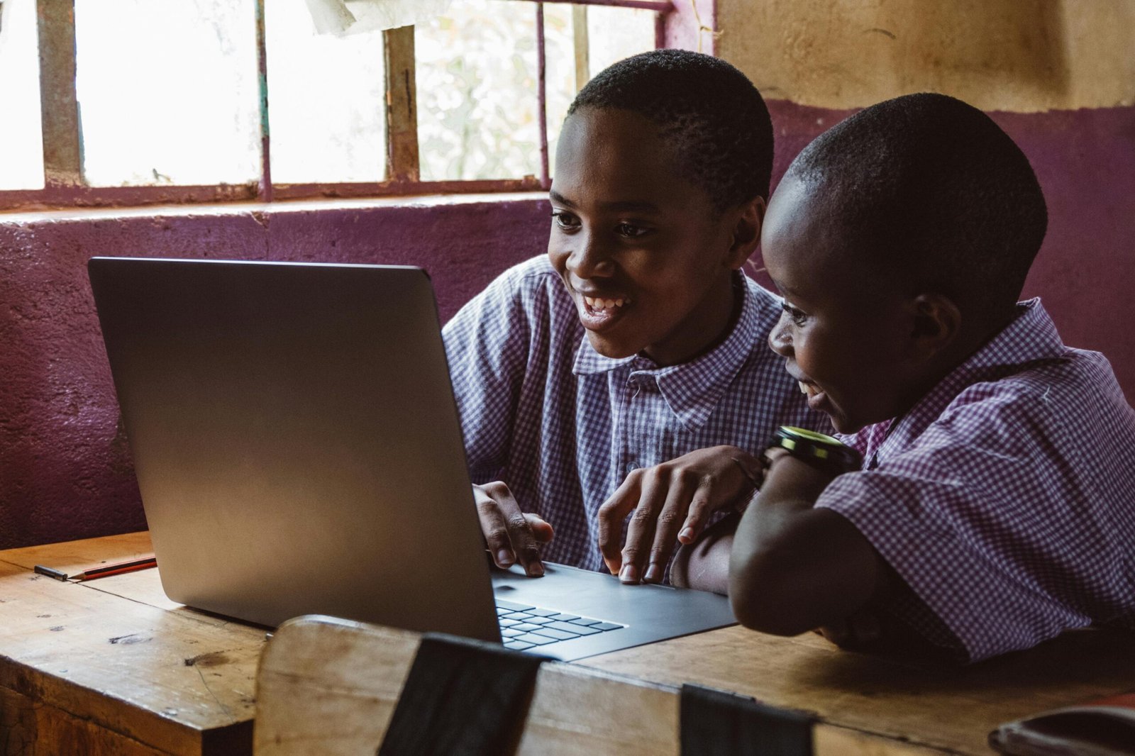 Smiling children learning together using a laptop indoors in a classroom setting.