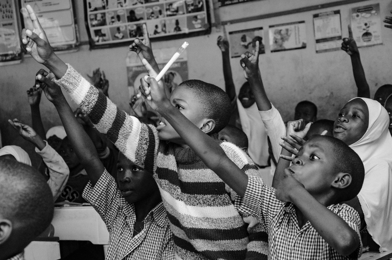 A vibrant black and white scene of young students eagerly participating in class, raising their hands.