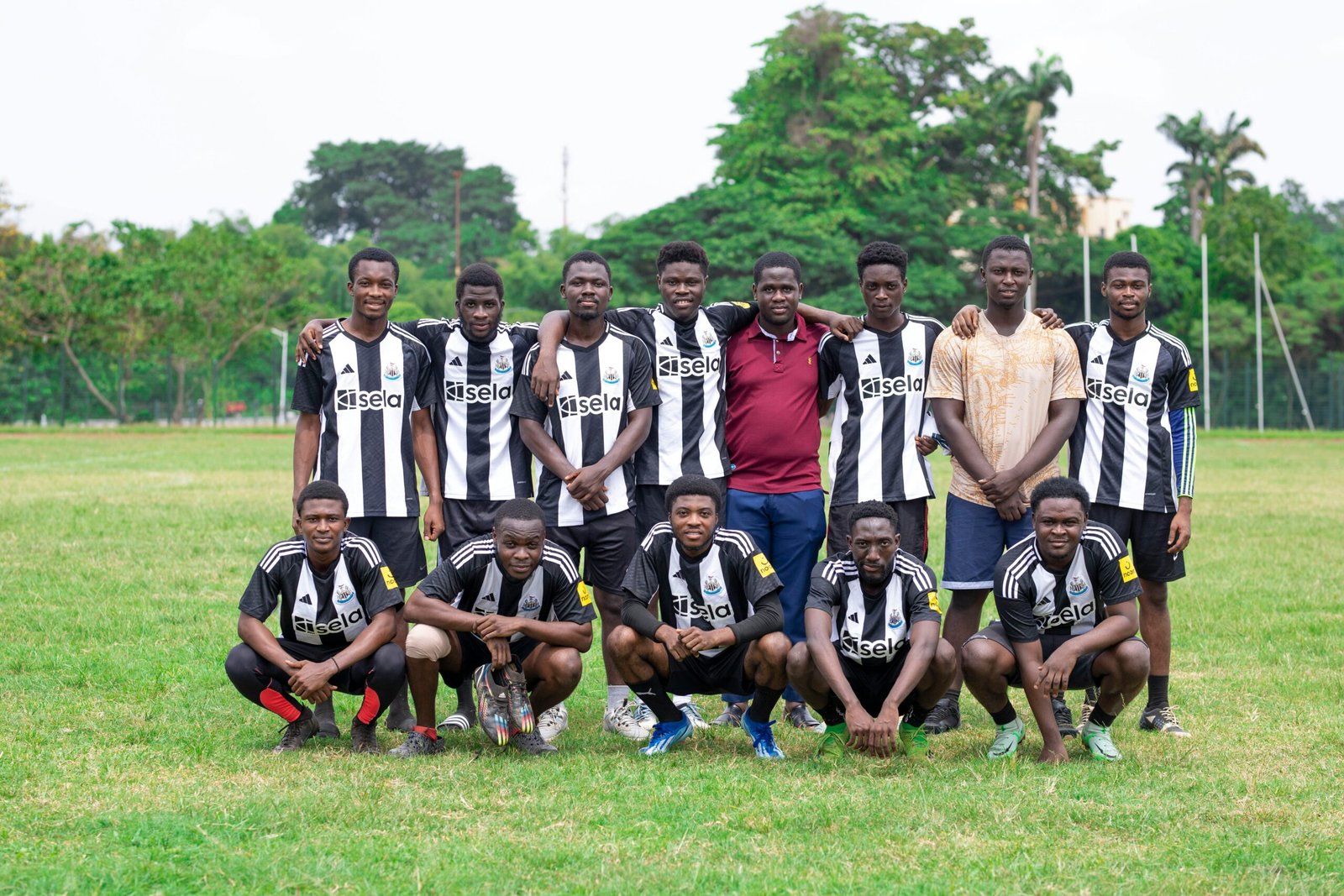 Youth soccer team in black and white jerseys posing together on a grassy field outdoors.
